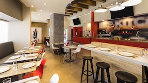 A modern restaurant with a bar area, high ceilings, and a mix of seating options including tables and stools.