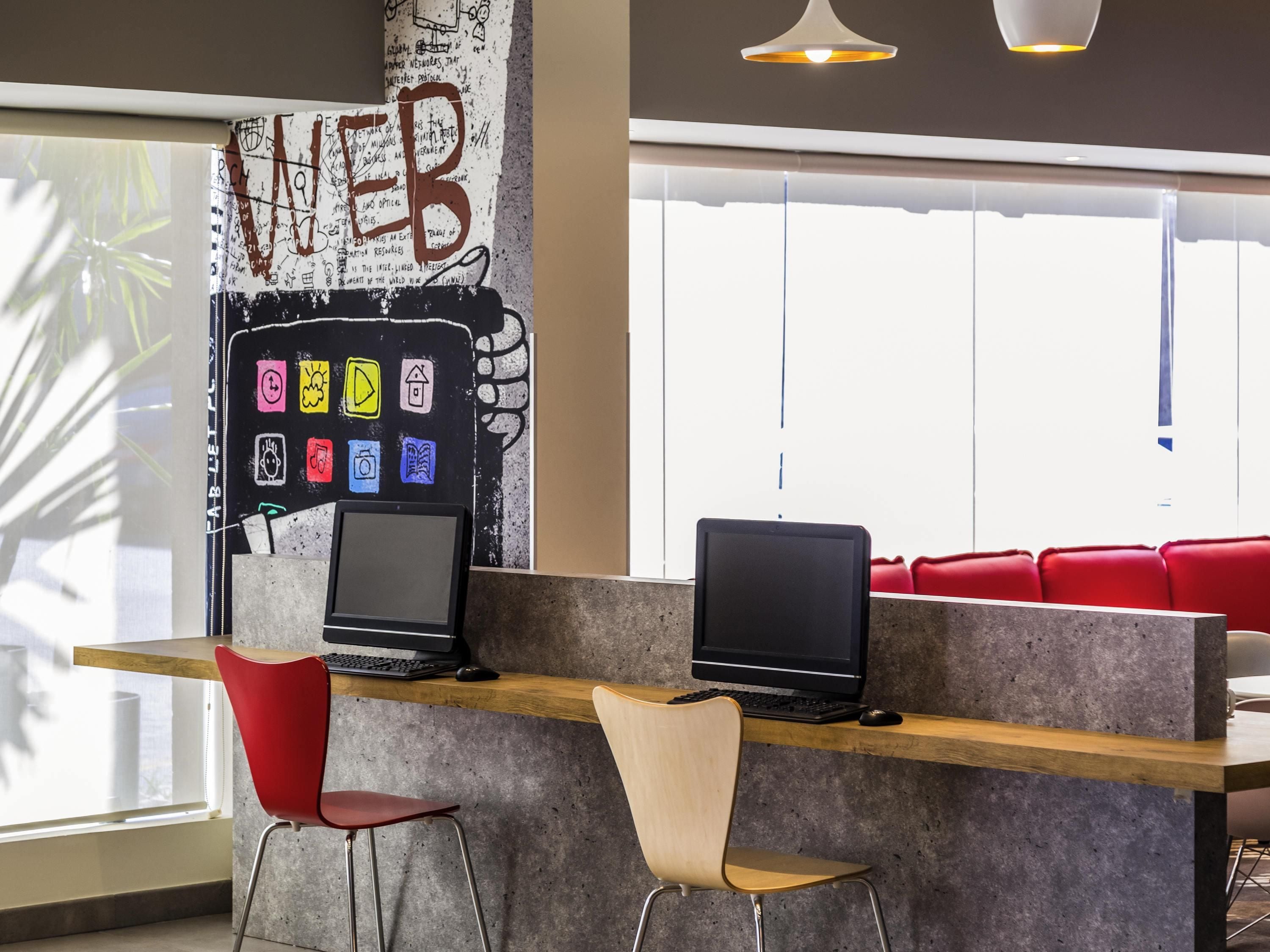 A modern workspace with two laptops on a wooden desk, two chairs, and a wall with a large 'WEB' sign.