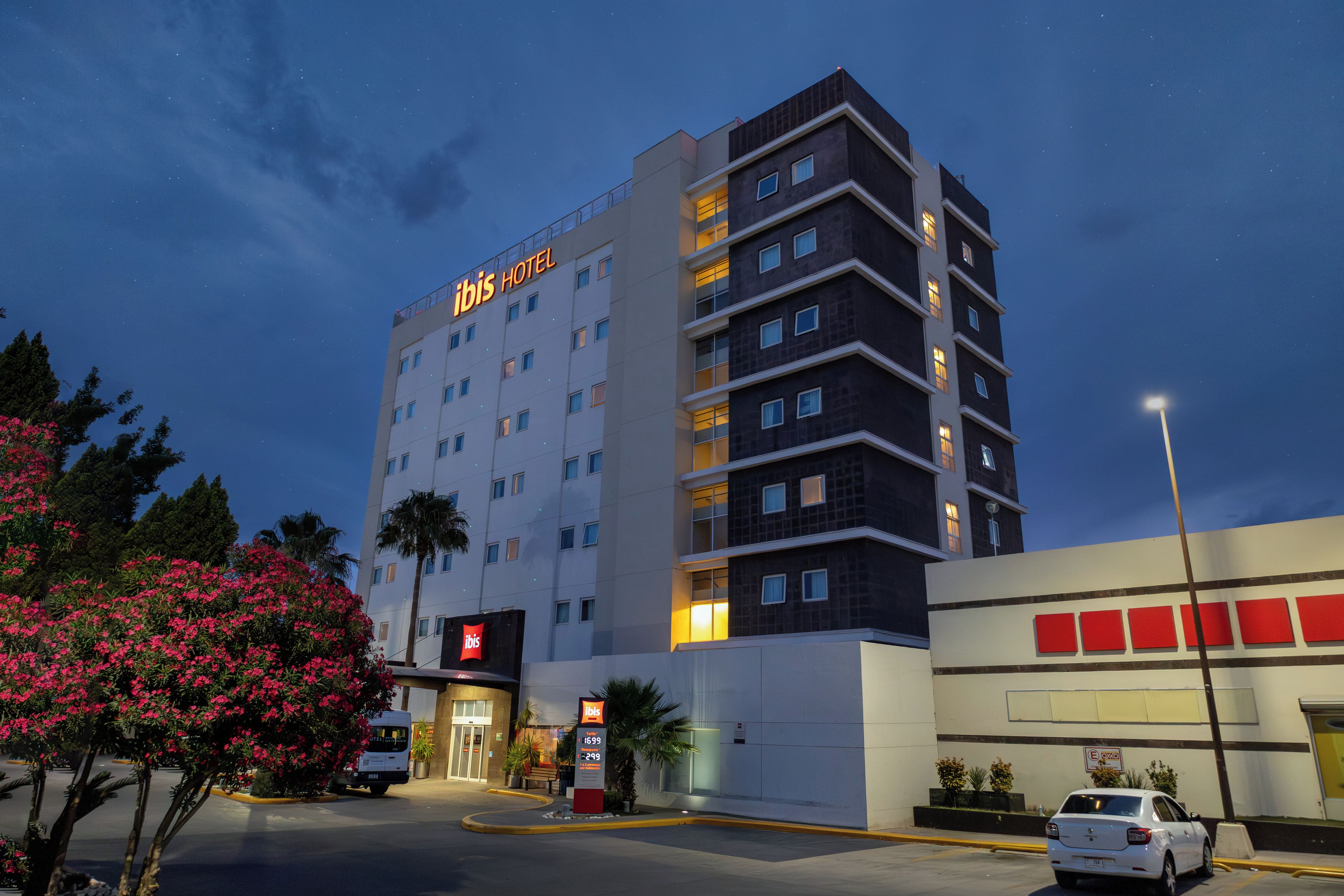 Un hôtel à plusieurs étages, reconnaissable à son grand panneau « ibis HOTEL », doté d’un parking et d’un lampadaire.