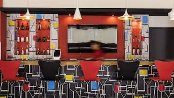 Una zona de bar con sillas rojas y negras, una pantalla de televisión grande y estantes con botellas.