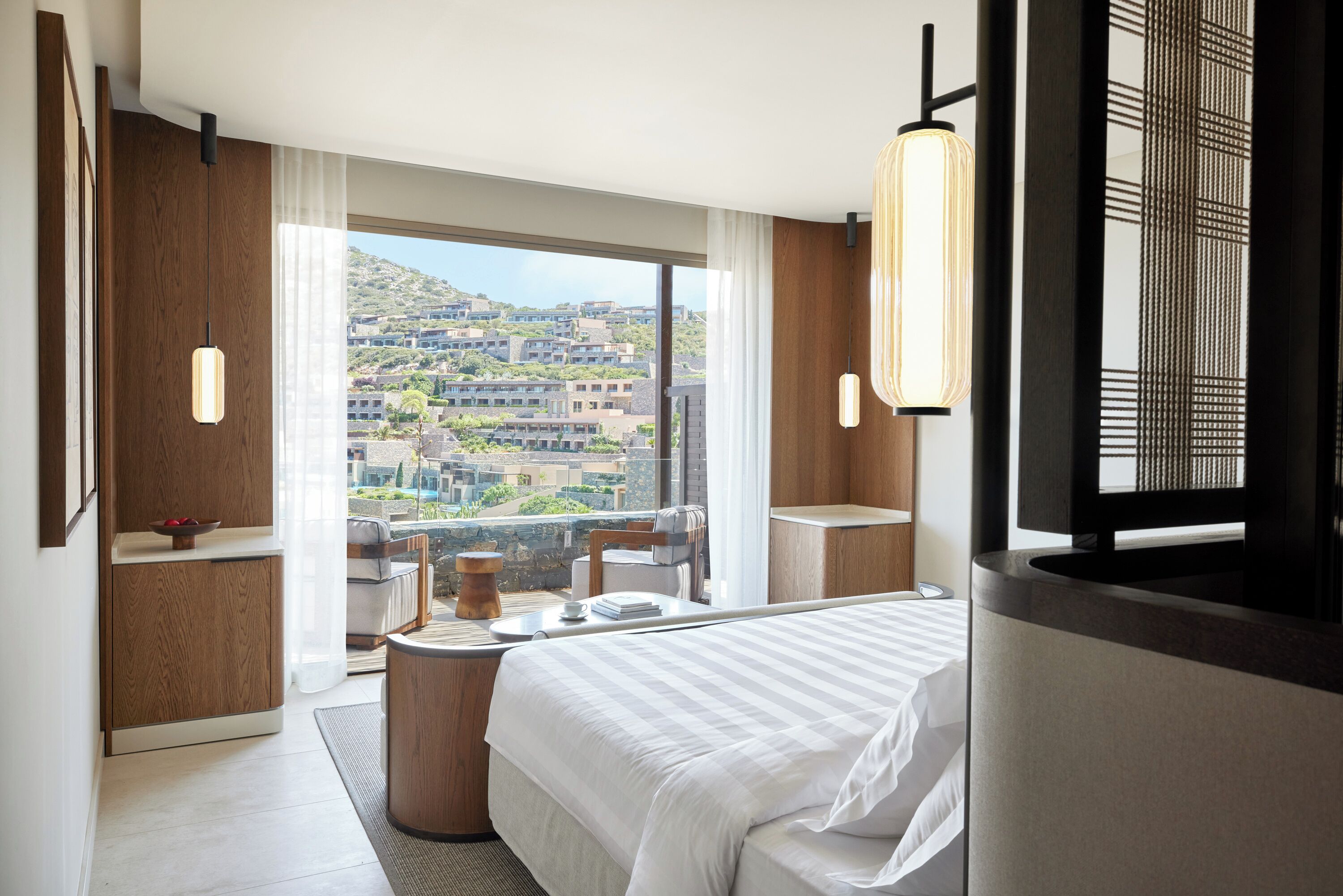 A modern hotel room with a large bed, a dining table, and a view of the cityscape.