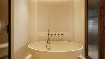 Un baño moderno con una bañera redonda grande, ducha empotrada y cerramiento de ducha de vidrio con marco de madera.
