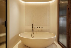 Un baño moderno con una bañera redonda grande, ducha empotrada y cerramiento de ducha de vidrio con marco de madera.