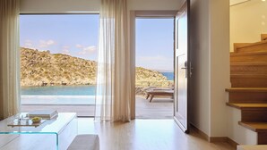 A modern room with a glass table, a view of the sea, and a wooden staircase. - Daios Cove (Agios Nikolaos)