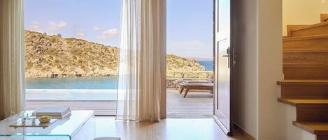 A modern room with a glass table, a view of the sea, and a wooden staircase.