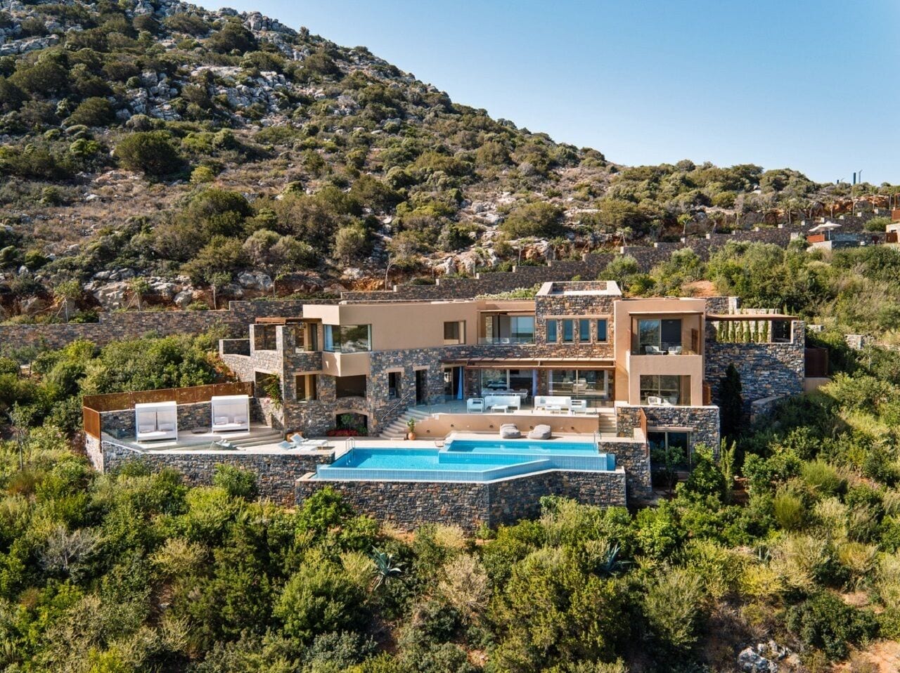 Una villa moderna con piscina, fachada de piedra y vistas a la colina.