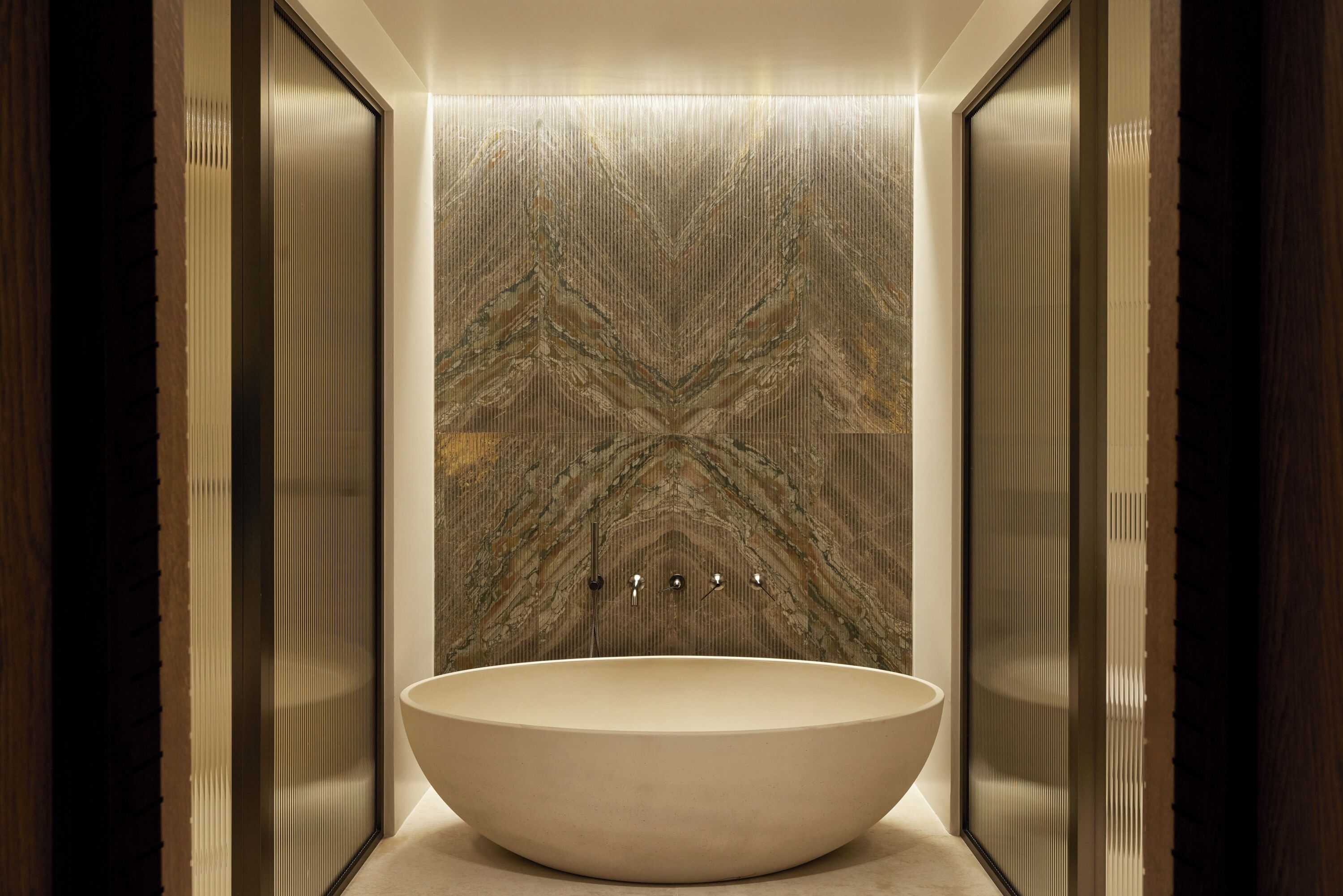A modern bathroom with a freestanding oval sink, a textured wall, and a wooden door frame.