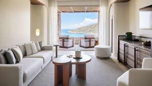 A modern living room with a sofa, two round tables, and a view of a coastal landscape. - Daios Cove (Agios Nikolaos)