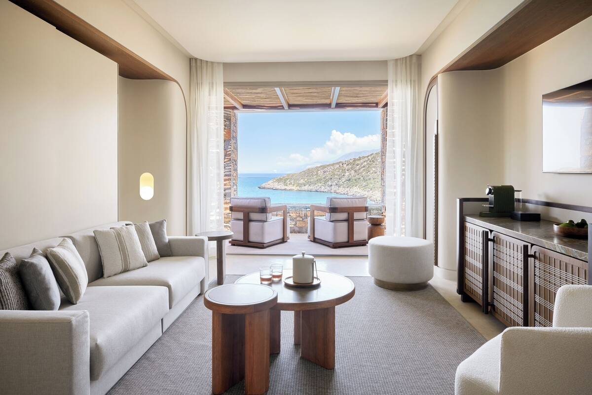 A modern living room with a sofa, two round tables, and a view of a coastal landscape.