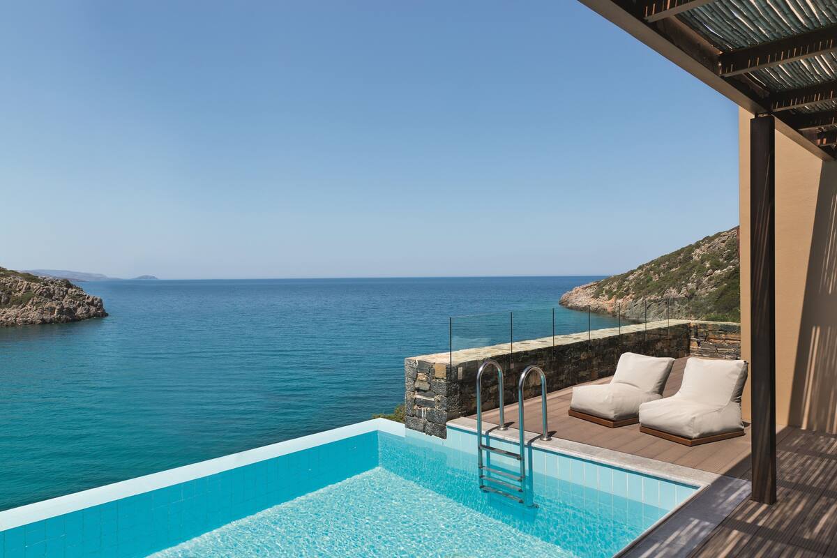 An infinity pool with a view of the sea, two white lounge chairs, and a stone wall.