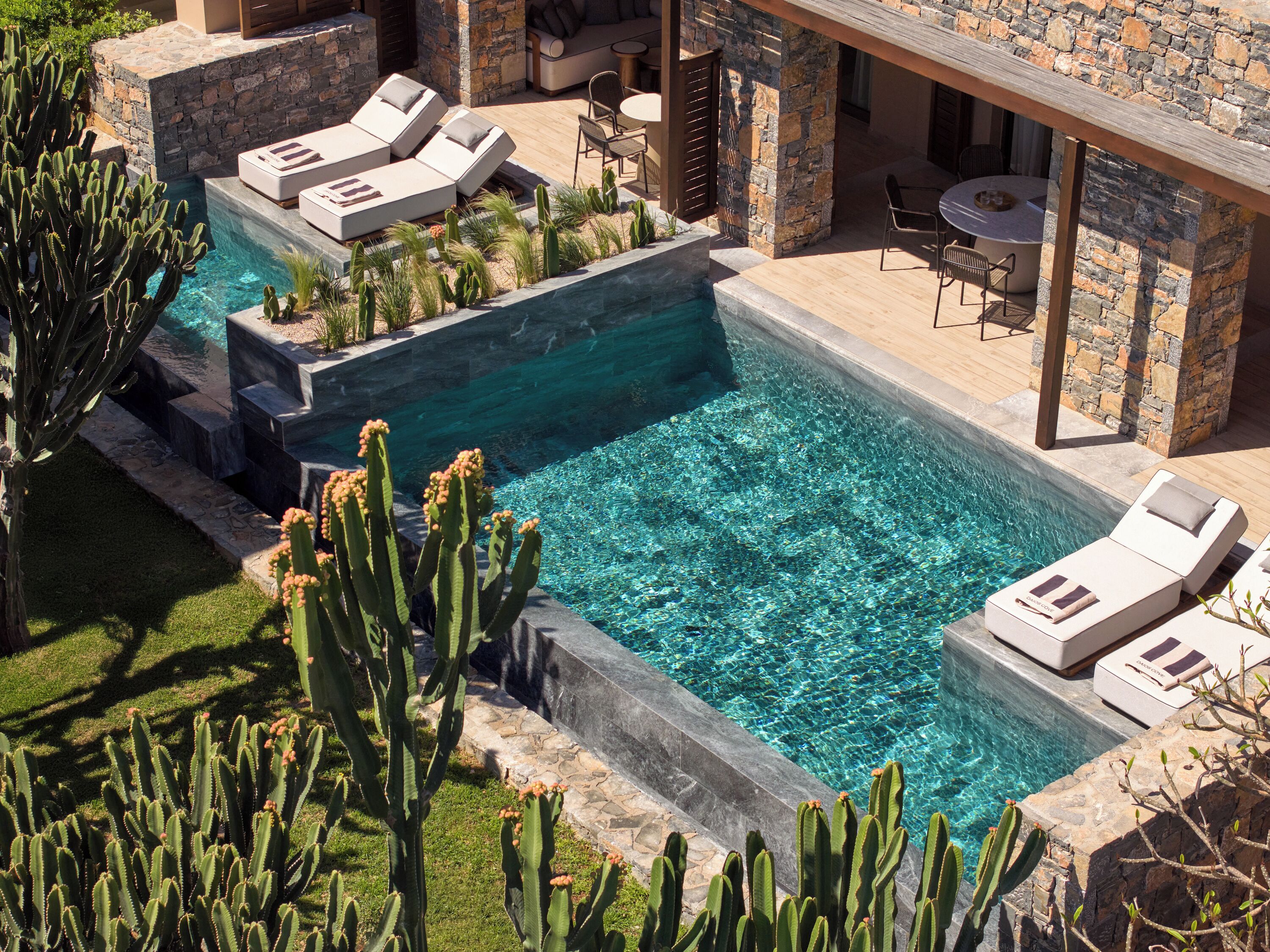 Un espace piscine agrémenté de chaises longues, d’un mur en pierre et de cactus.
