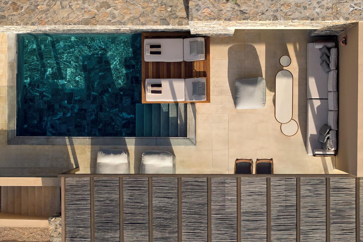 An aerial view of a modern outdoor pool area with lounge chairs, a sun lounger, and a stone wall.