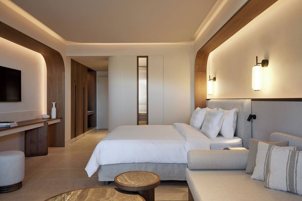 A modern hotel room with a large bed, a sofa, a small round table, and a TV mounted on the wall.