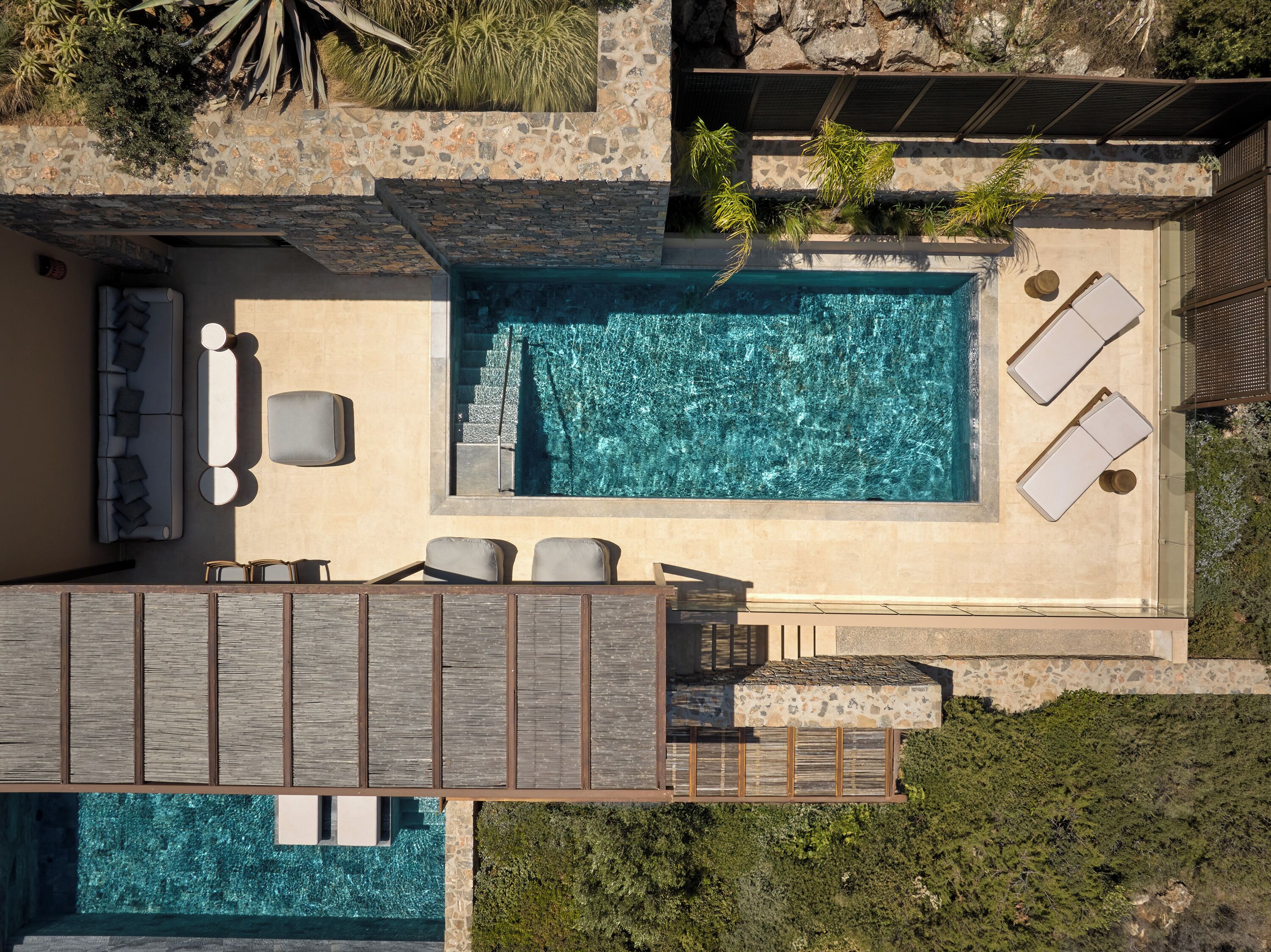 Vue aérienne d’un complexe hôtelier moderne doté d’une grande piscine, de chaises longues et d’une terrasse en bois.
