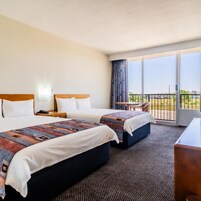 Habitación de hotel con dos camas, un balcón con vistas y un escritorio.
