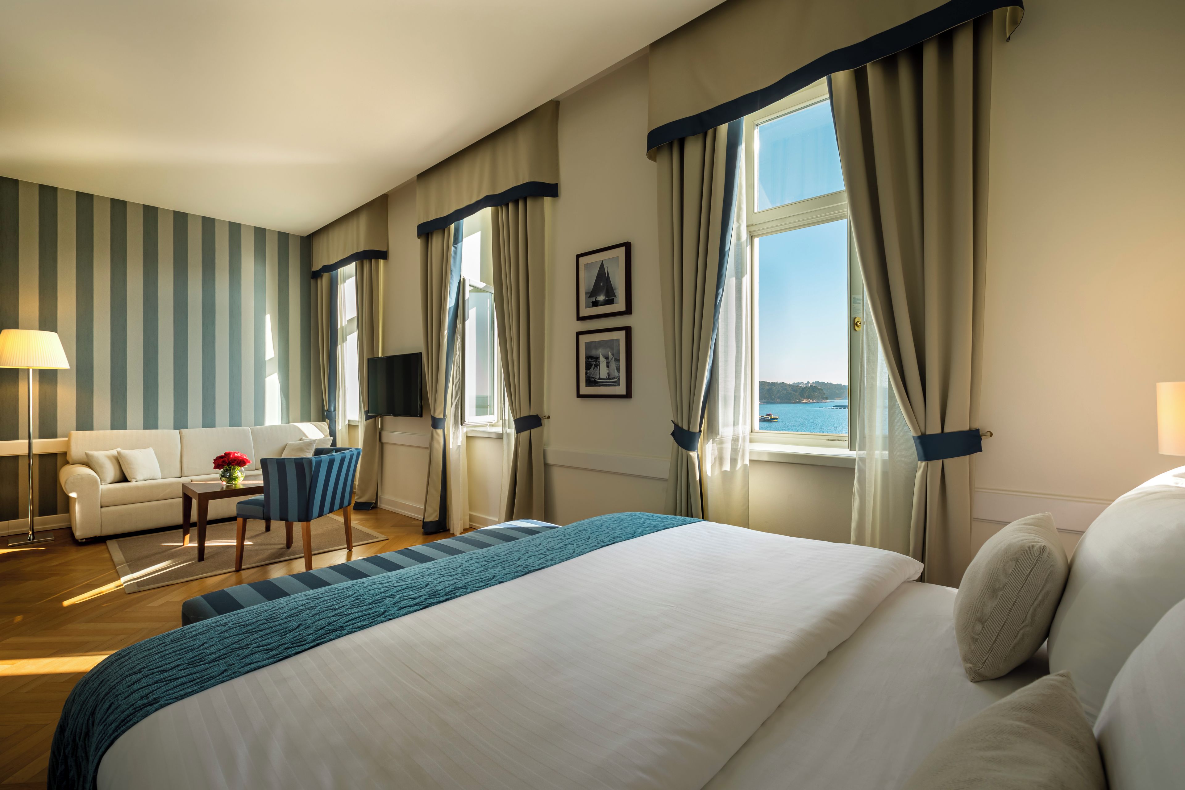 A hotel room with a large bed, a sofa, a chair, a desk, and a view of the sea.