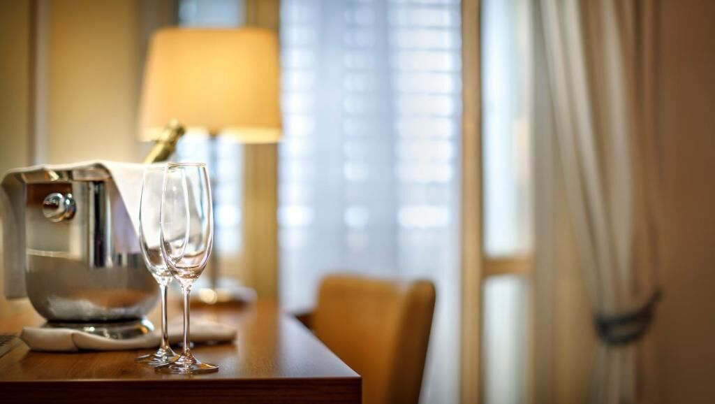 Une chambre d’hôtel avec une table en bois, deux verres à vin, une machine à café et une lampe.