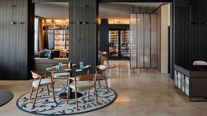 A modern hotel lobby with a round dining table, chairs, and a bar area with shelves of bottles. - Valamar Riviera Hotel & Residence (Porec)