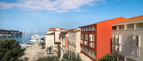 A coastal hotel with multiple balconies, a marina with boats, and a clear blue sky.