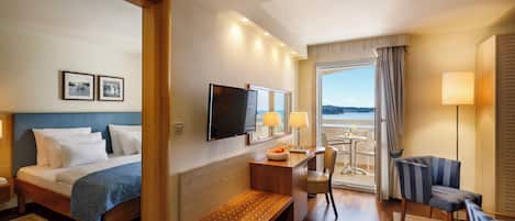 A hotel room with a bed, desk, chair, and a view of the sea.