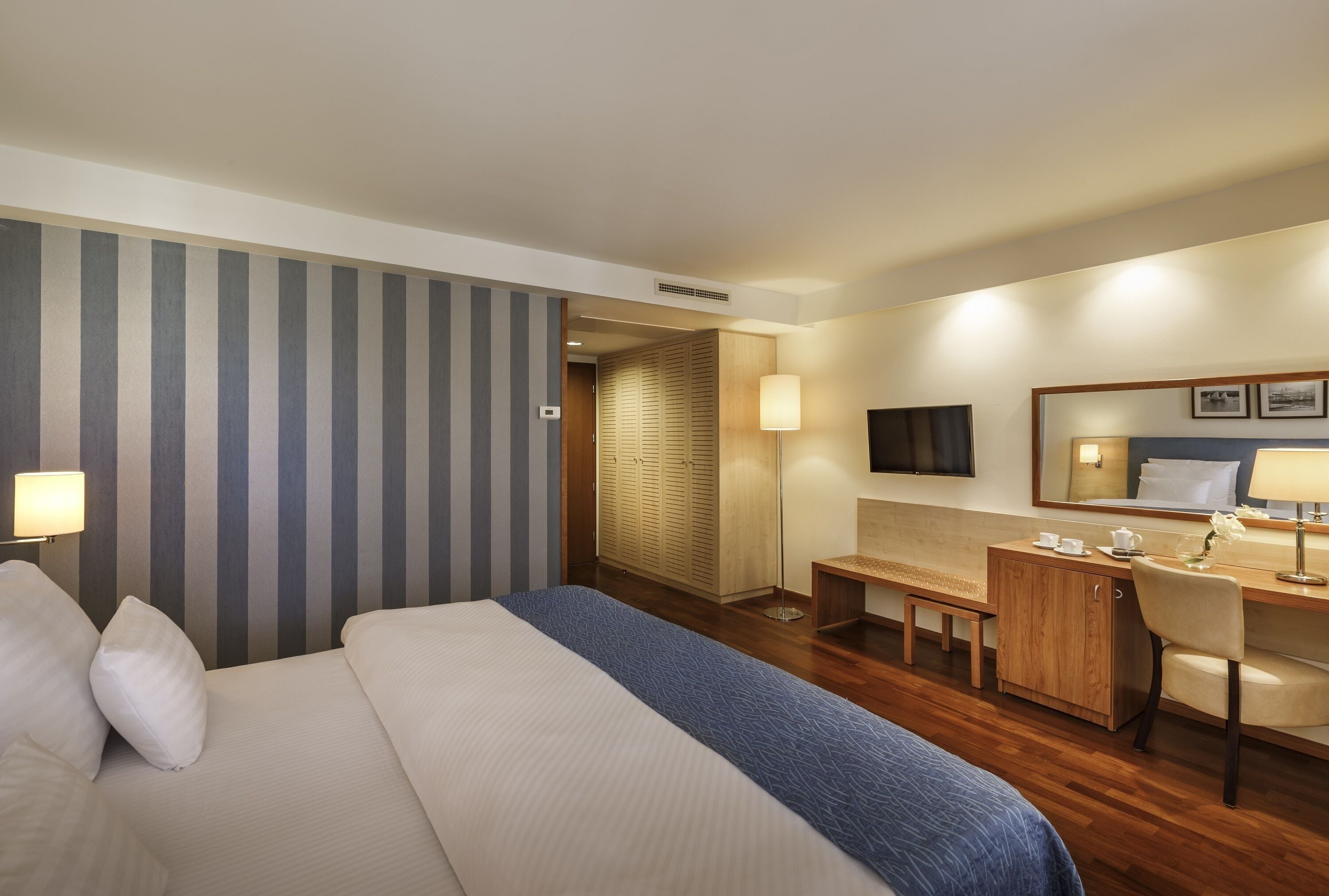 Ein Hotelzimmer mit einem großen Bett, einem Schreibtisch, einem Sessel, einer Lampe, einem Spiegel und einem Kleiderschrank.