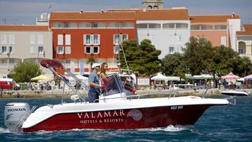 Ein Boot mit dem Namen 'VALAMAR HOTELS & RESORTS' und der Aufschrift '102 ND', das sich auf dem Wasser bewegt, mit einer Stadtlandschaft im Hintergrund.