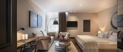 A modern hotel room with a sofa, a bed, a desk with a lamp, and a coffee table.
