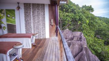 A wooden deck with massage tables, a woven wall, and a view of lush greenery.