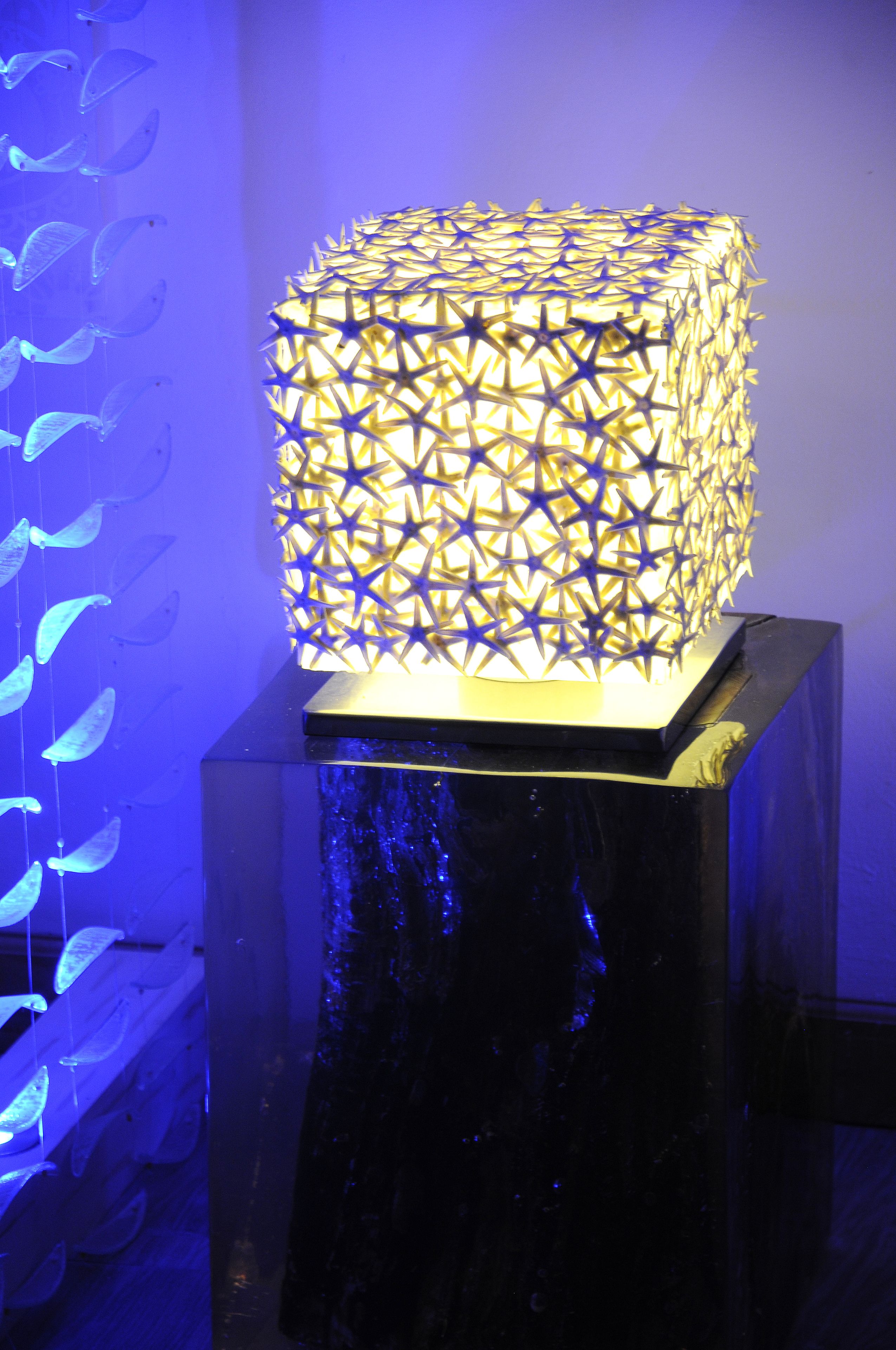A decorative cube-shaped light fixture with a star-like pattern, placed on a black pedestal.