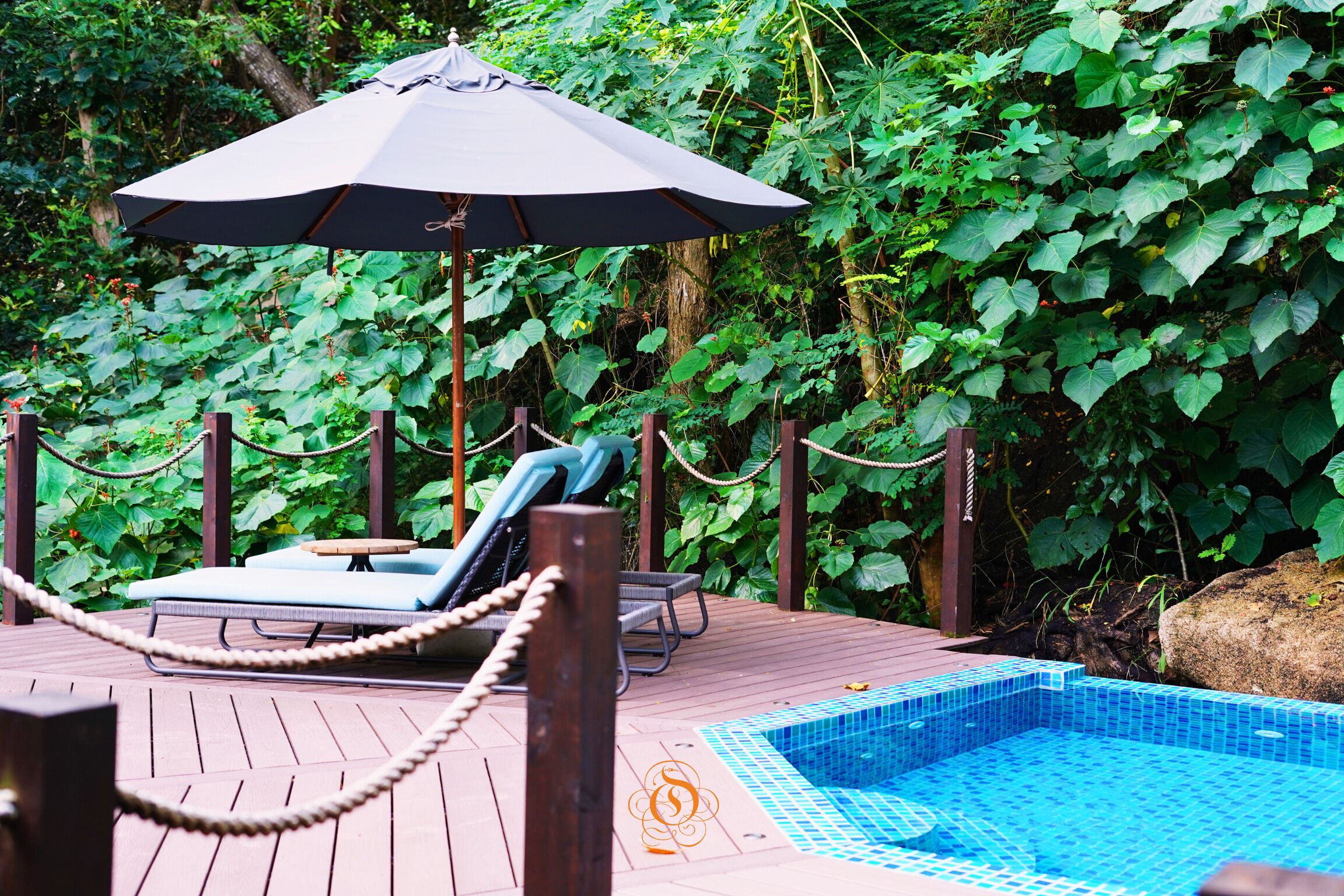 A wooden deck with a pool, lounge chairs, and an umbrella.