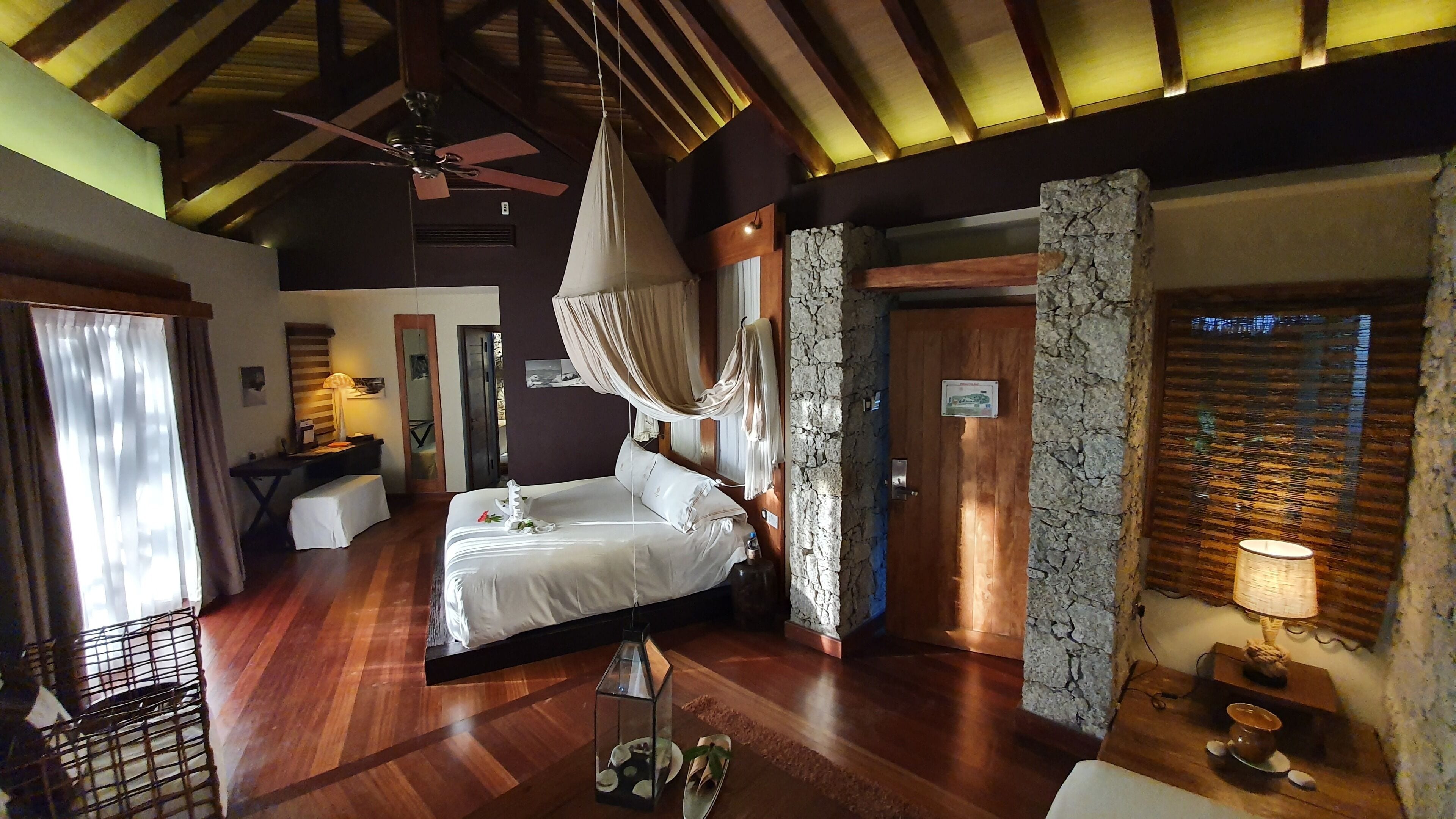 A bedroom with a bed, bedside table, lamp, and a view of the outside.