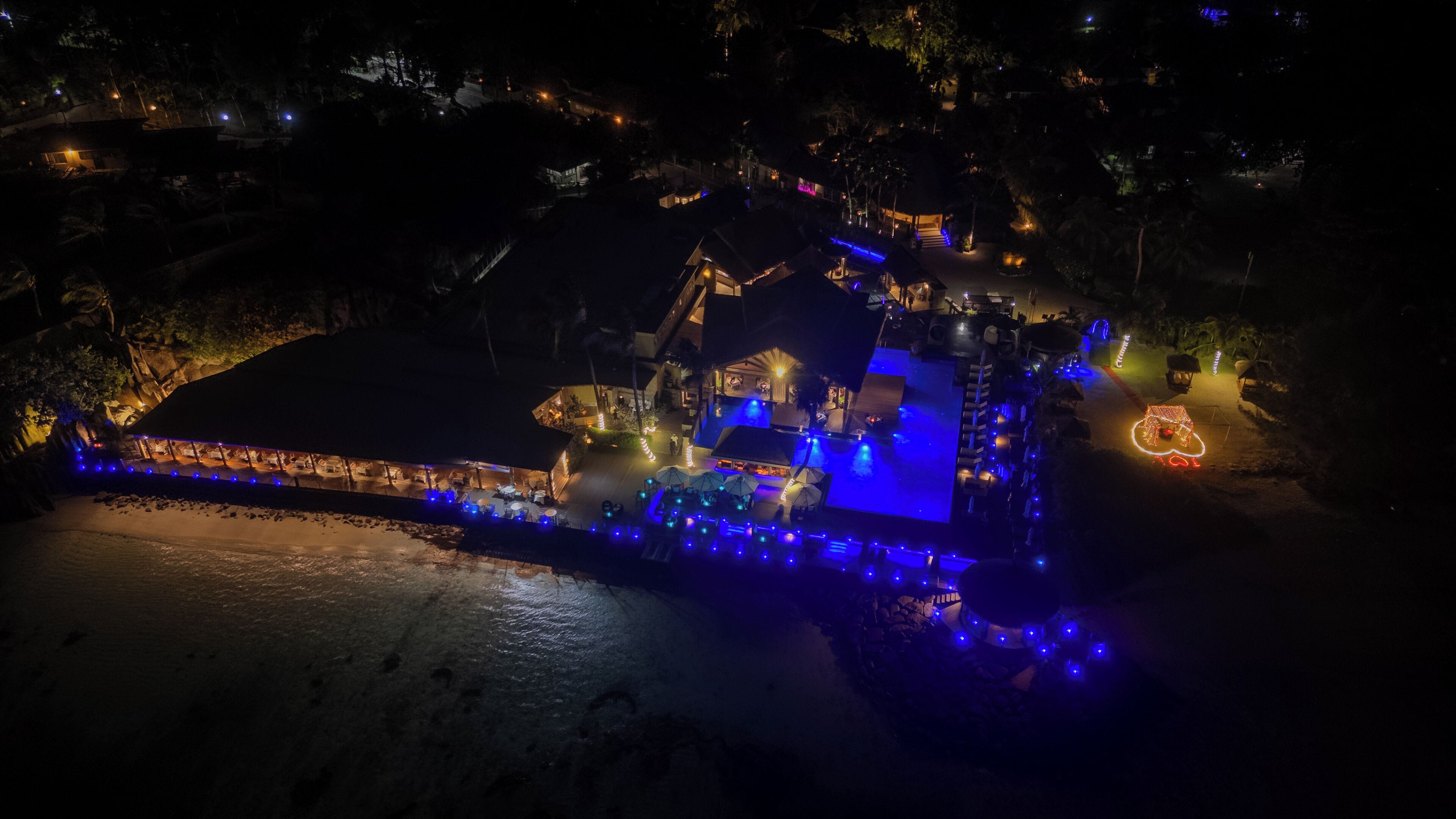 An aerial view of a resort with a pool, outdoor seating, and illuminated pathways.
