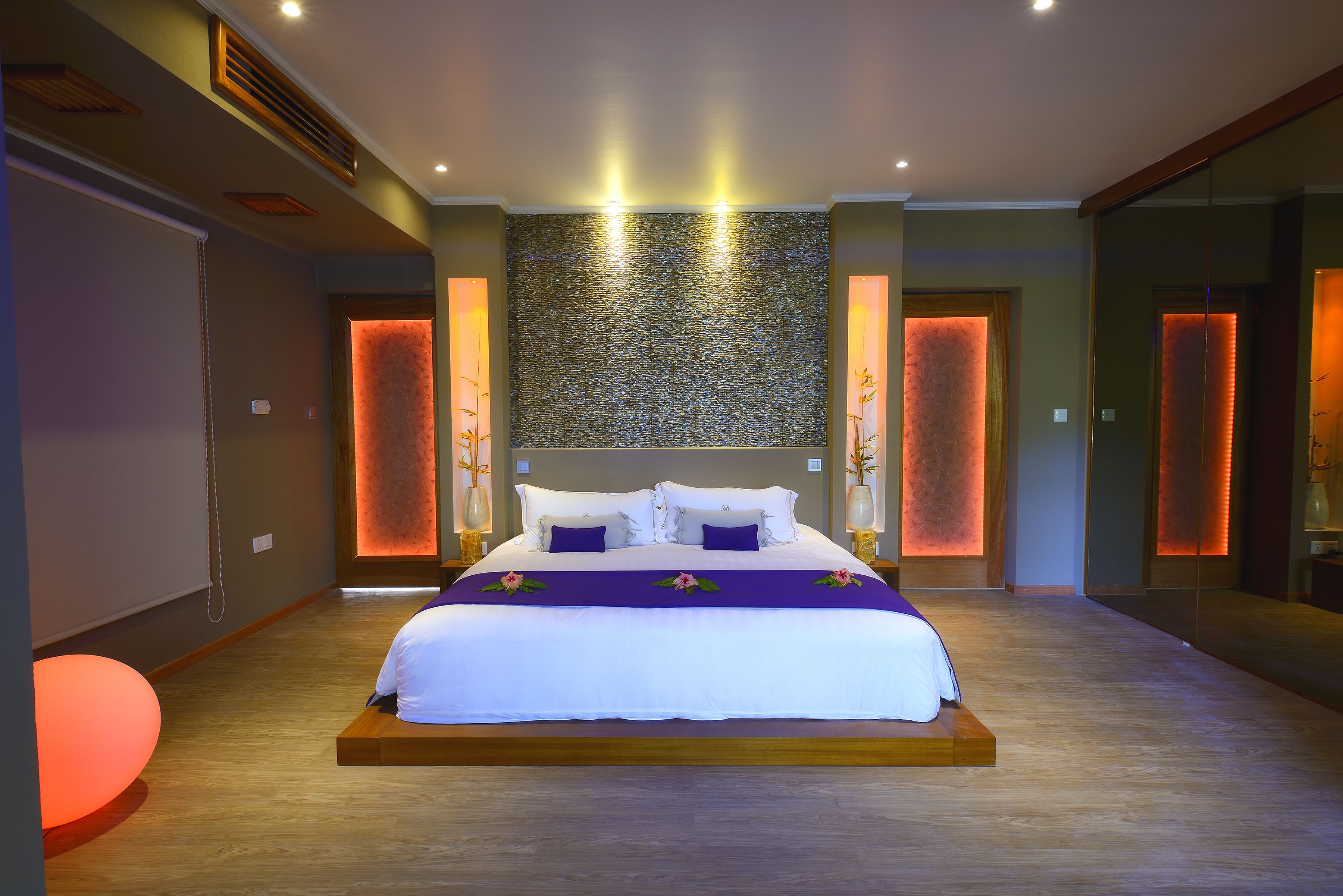 A modern hotel room with a large bed, wooden flooring, and a textured wall behind the bed.