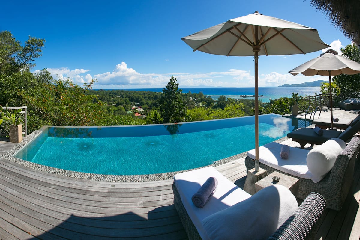 Une piscine privée à débordement, dotée d’une terrasse en bois, de chaises longues et de parasols.