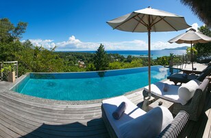 Piscina infinita privada con terraza de madera, sillas de descanso y sombrillas.