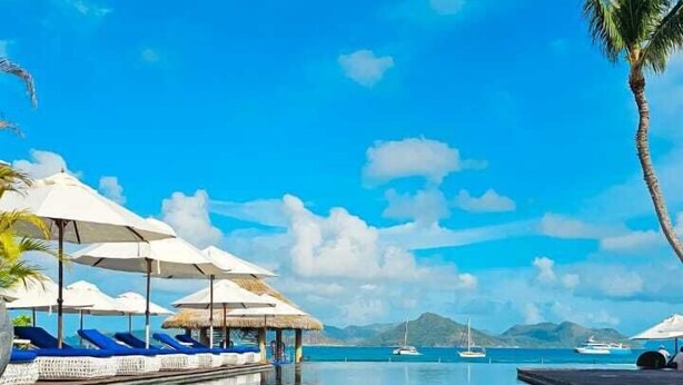 Un ciel d’un bleu limpide, une piscine tranquille et des chaises longues avec des parasols.
