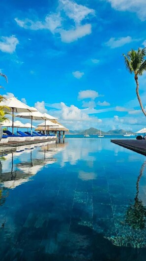 Un ciel d’un bleu limpide, une piscine tranquille et des chaises longues avec des parasols.