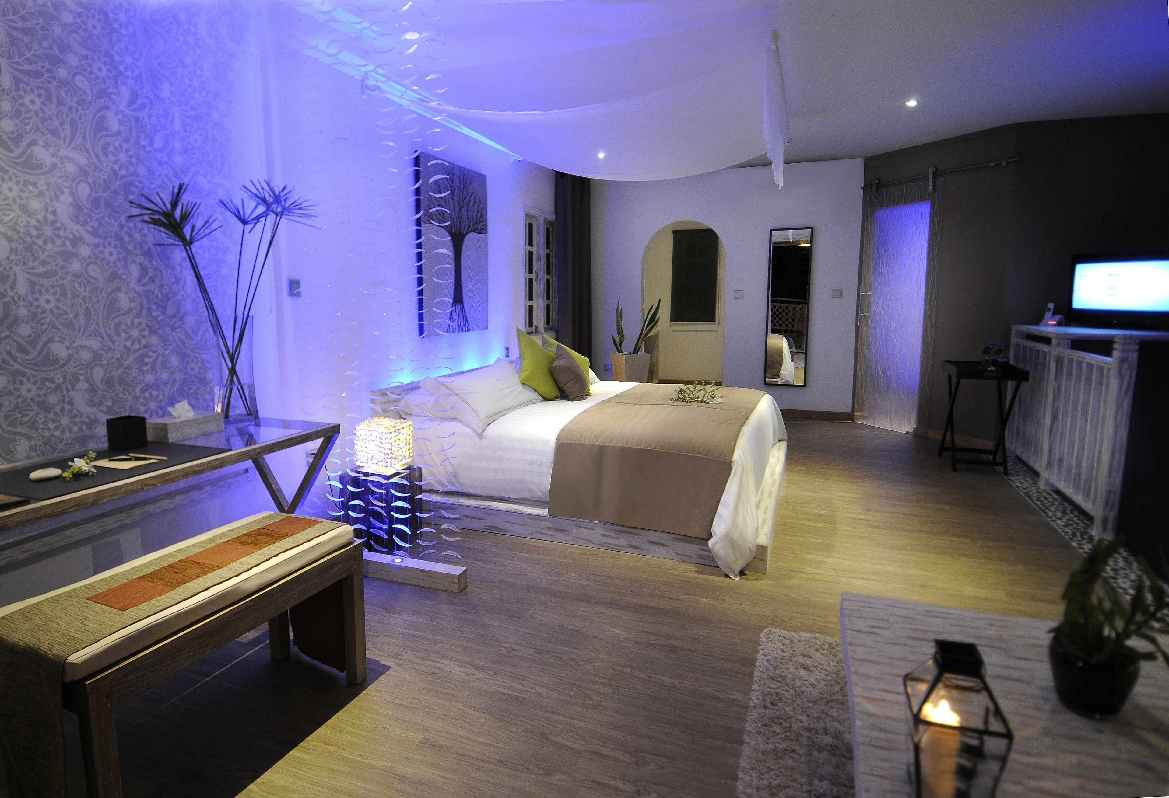 A modern bedroom with a large bed, bedside tables, a bench, and a TV.