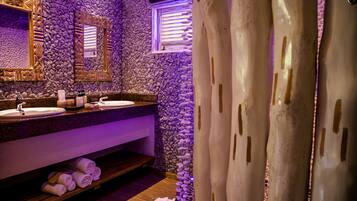 A bathroom with a stone wall, two sinks, a mirror, and a window with blinds.