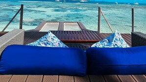 Une terrasse en bois avec des coussins bleus et une vue sur l’océan et les îles lointaines.