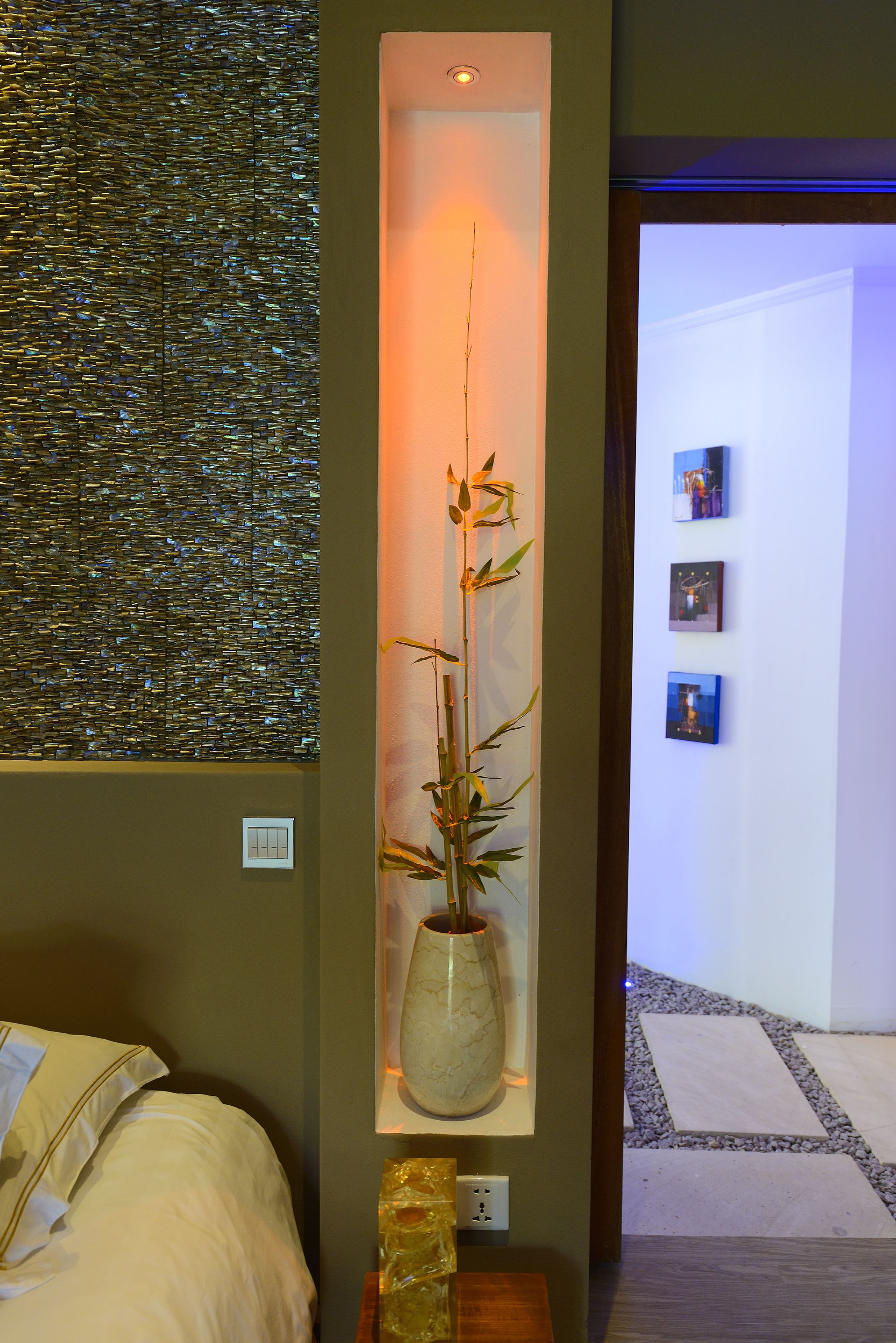 A room with a bed, a wall-mounted shelf with a vase, and a textured wall.