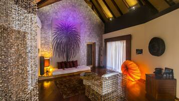 Una habitación acogedora con pared de piedra, una cama con almohadones rojos, una silla de mimbre y un paraguas grande.