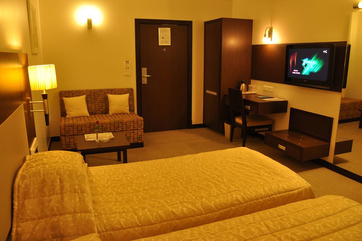 A hotel room with a bed, a sofa, a desk, and a television.