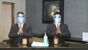 Dos personas sentadas a una mesa con un dispensador de gel antibacterial y una caja de pañuelos.