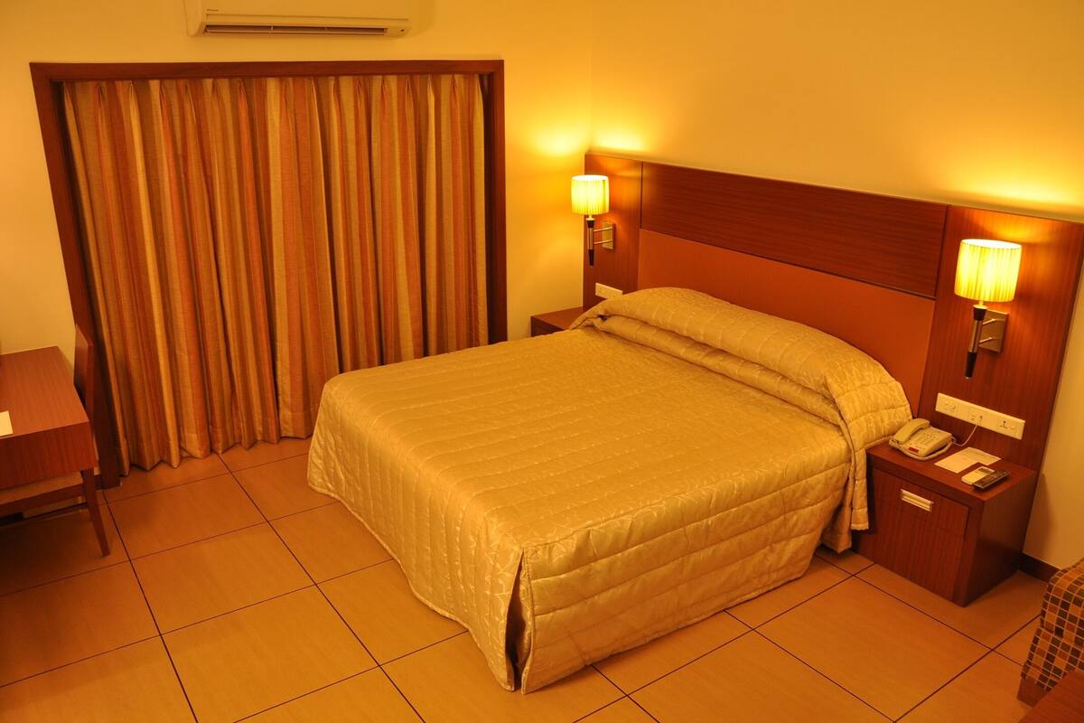 A hotel room with a large bed, two bedside lamps, a nightstand with a phone, and a curtain.