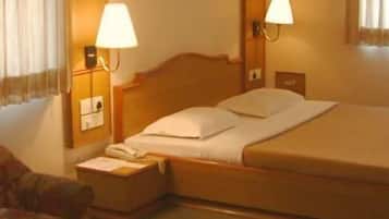 Habitación de hotel con una cama individual, dos lámparas de noche, una mesita de noche con un teléfono, una pequeña mesa con una taza y una silla.