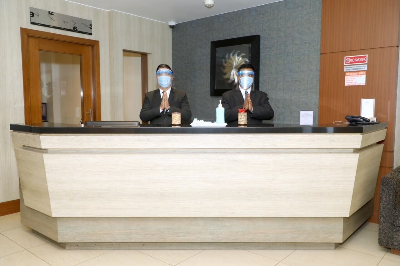 A reception desk with two individuals seated behind it, a clock, a 'No Smoking' sign, and a framed artwork on the wall.