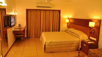 A hotel room with a bed, bedside table, lamp, TV, and curtains.
