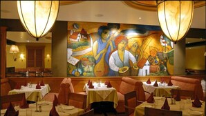 Un restaurante con mesas dispuestas para comer, un mural en la pared y dos lámparas grandes colgantes.