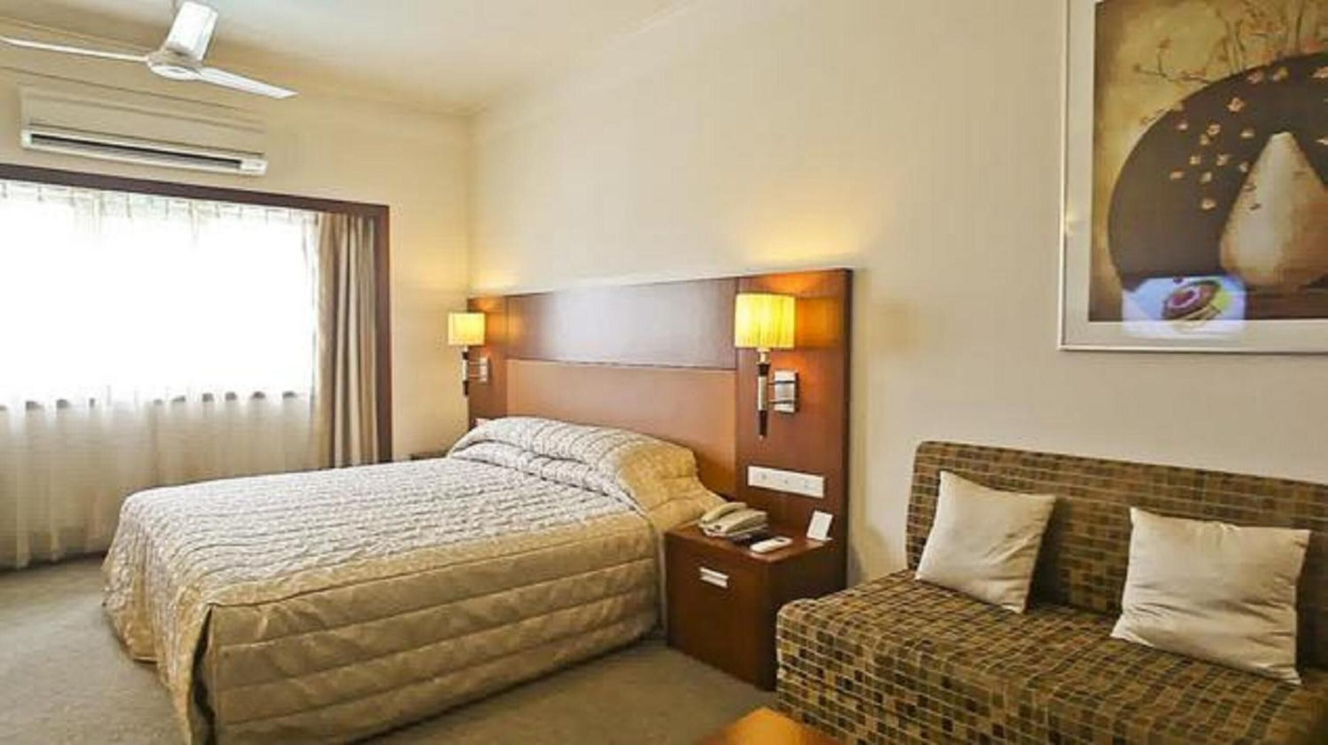 Una habitación de hotel con cama, sofá, mesita de noche y lámpara de pared.
